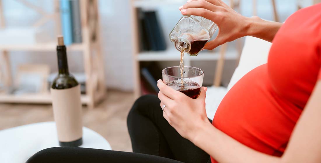 беременная женщина сидит на диване и наливает себе алкоголь